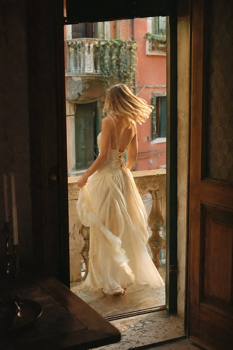 Woman in cream dress twirls on a sunlit Venetian balcony