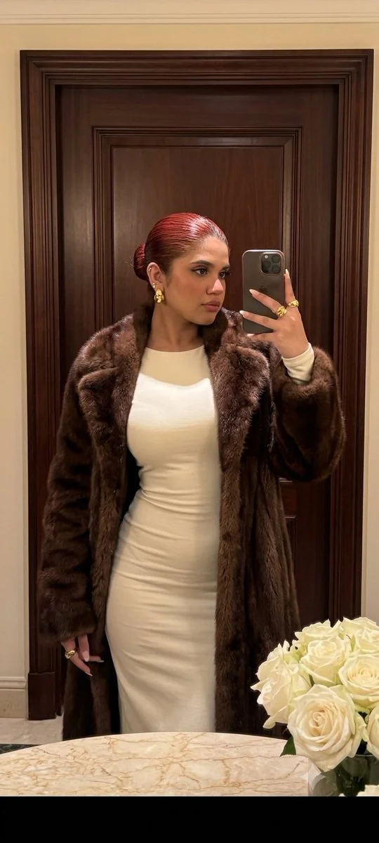 Woman in fur coat checks her reflection in classic interior
