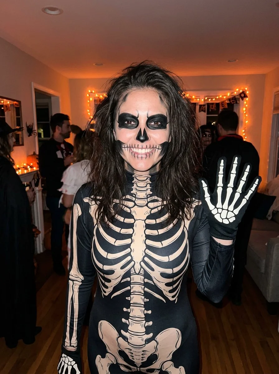 Woman in skeleton bodysuit poses at a lively Halloween house party