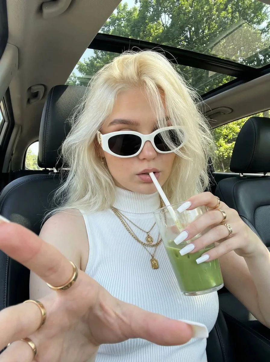 Woman in white top captures selfie with green drink in car