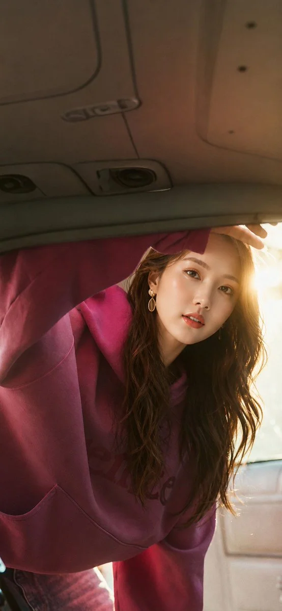 Woman leans into car trunk as golden sunlight streams through