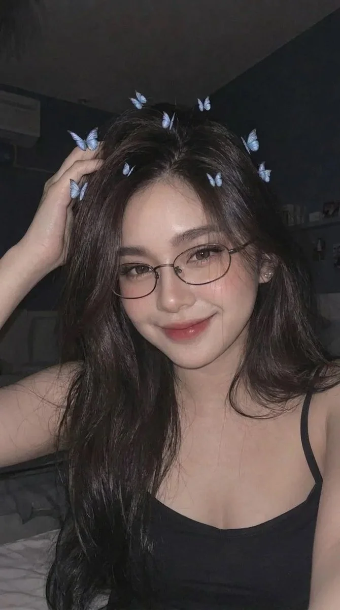 Woman with long dark hair and glasses smiles softly in low light