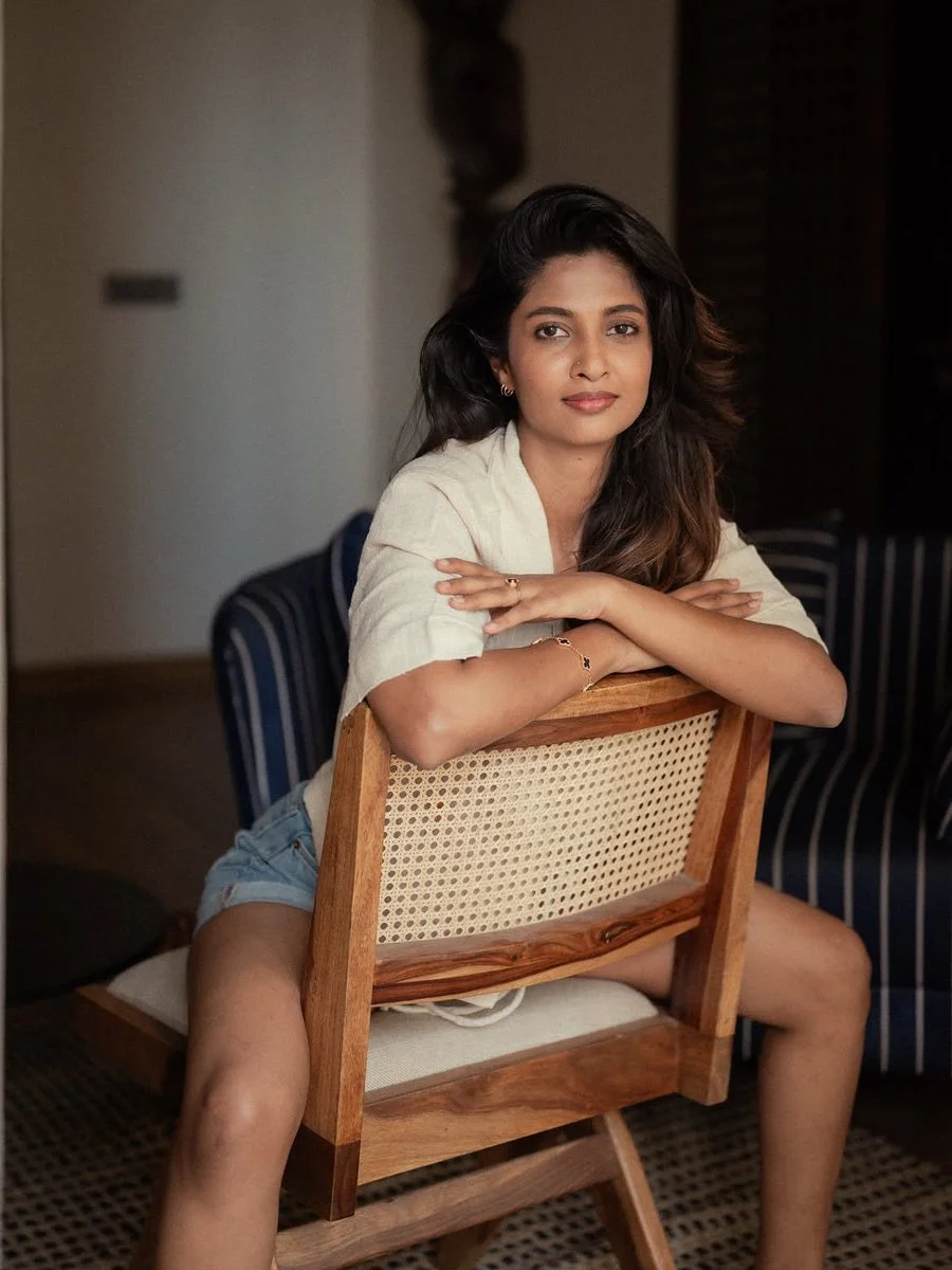 Young Indian woman rests arms on wooden chair in warm light