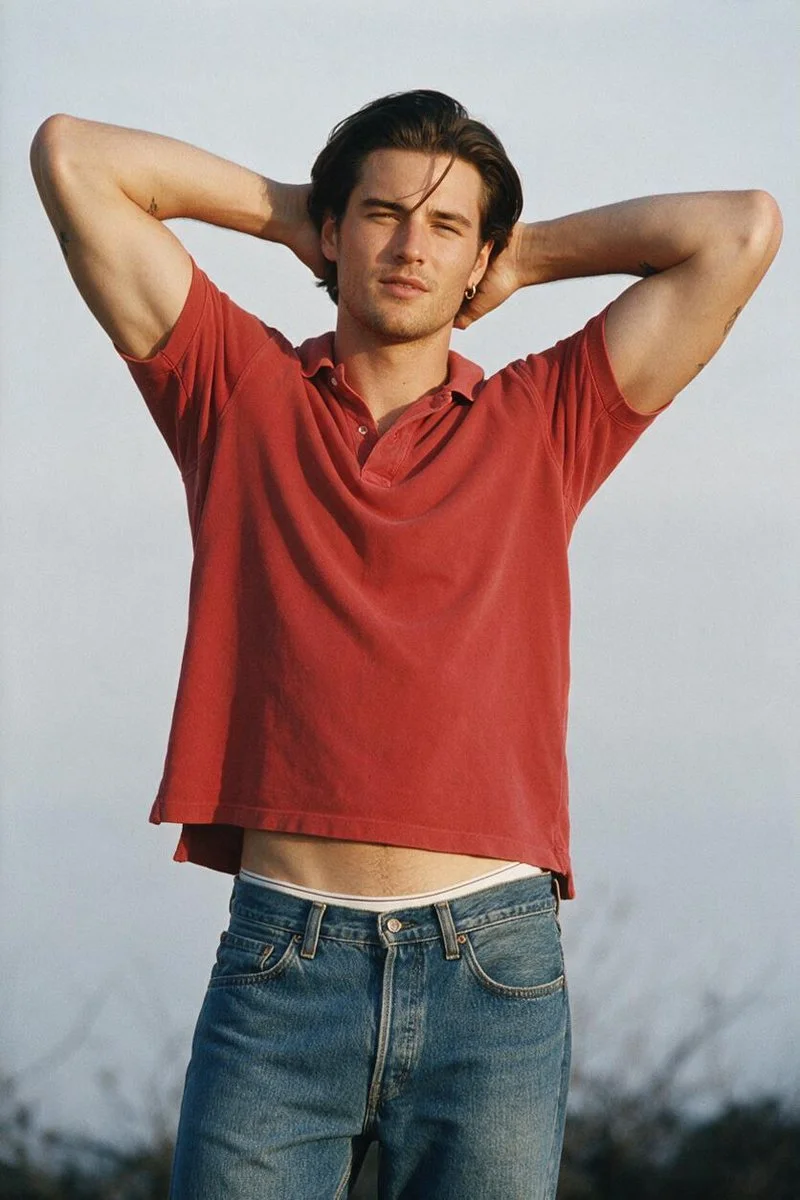 Young man poses with arms behind head under pale sky in 35mm editorial style