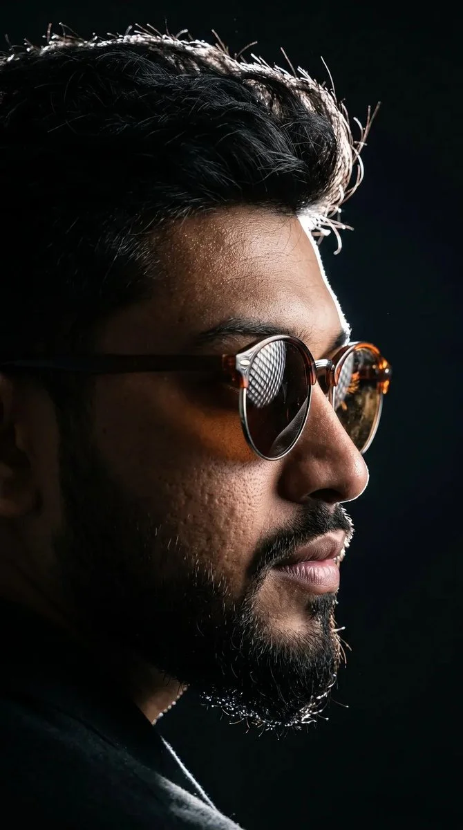 Young man's profile emerges from darkness with rim-lit sunglasses