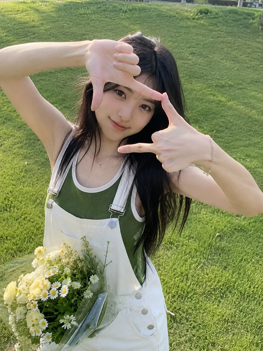 Young woman frames her smiling face with hands on sunny lawn