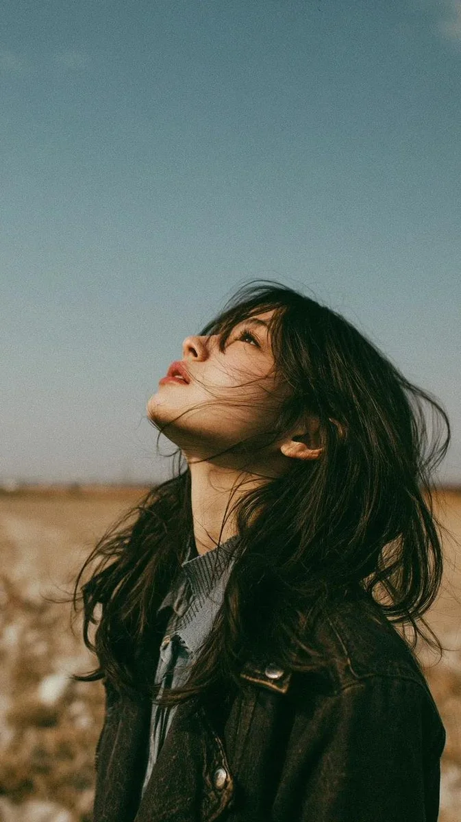 Young woman in autumn meadow gazes at blue sky, wind in hair