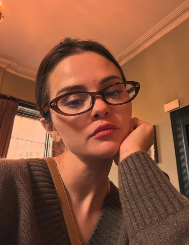 Young woman in tortoiseshell glasses rests chin on hand thoughtfully