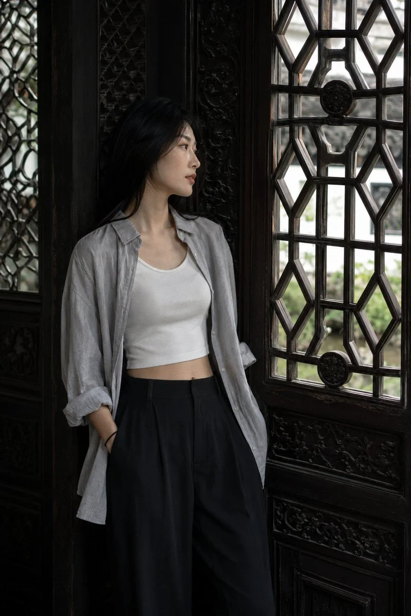 Young woman leans beside carved lattice window in dim hall