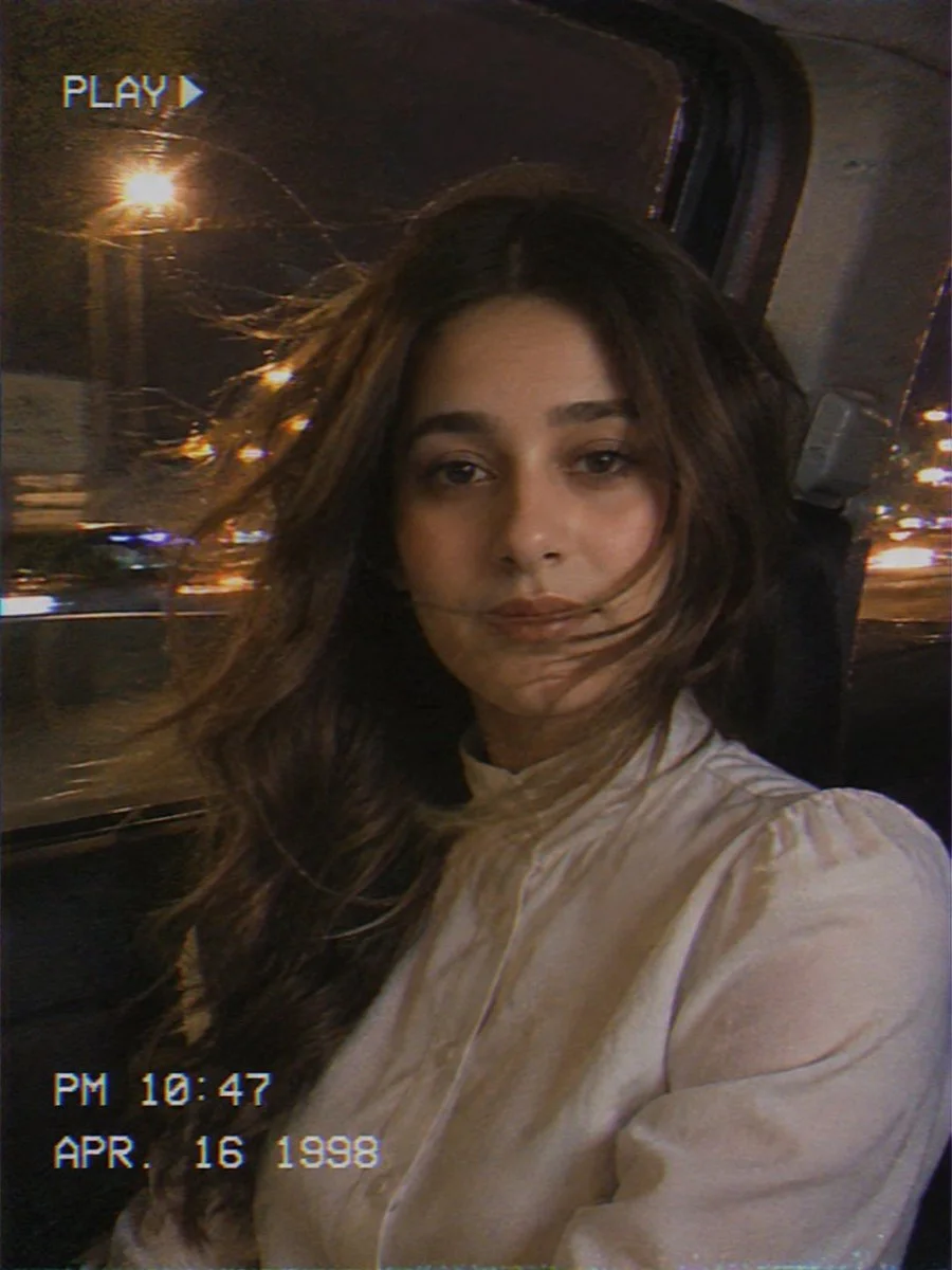 Young woman rides in backseat with city lights streaming behind her.