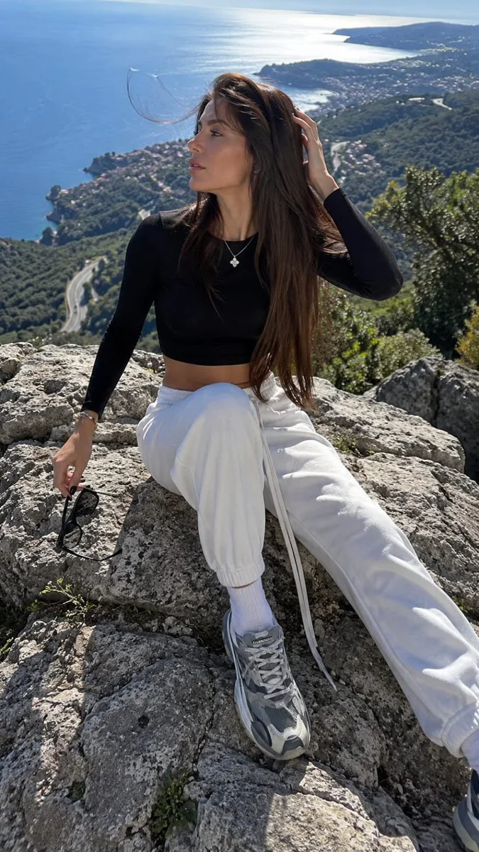 Young woman sits on coastal rock with windblown hair and distant sea