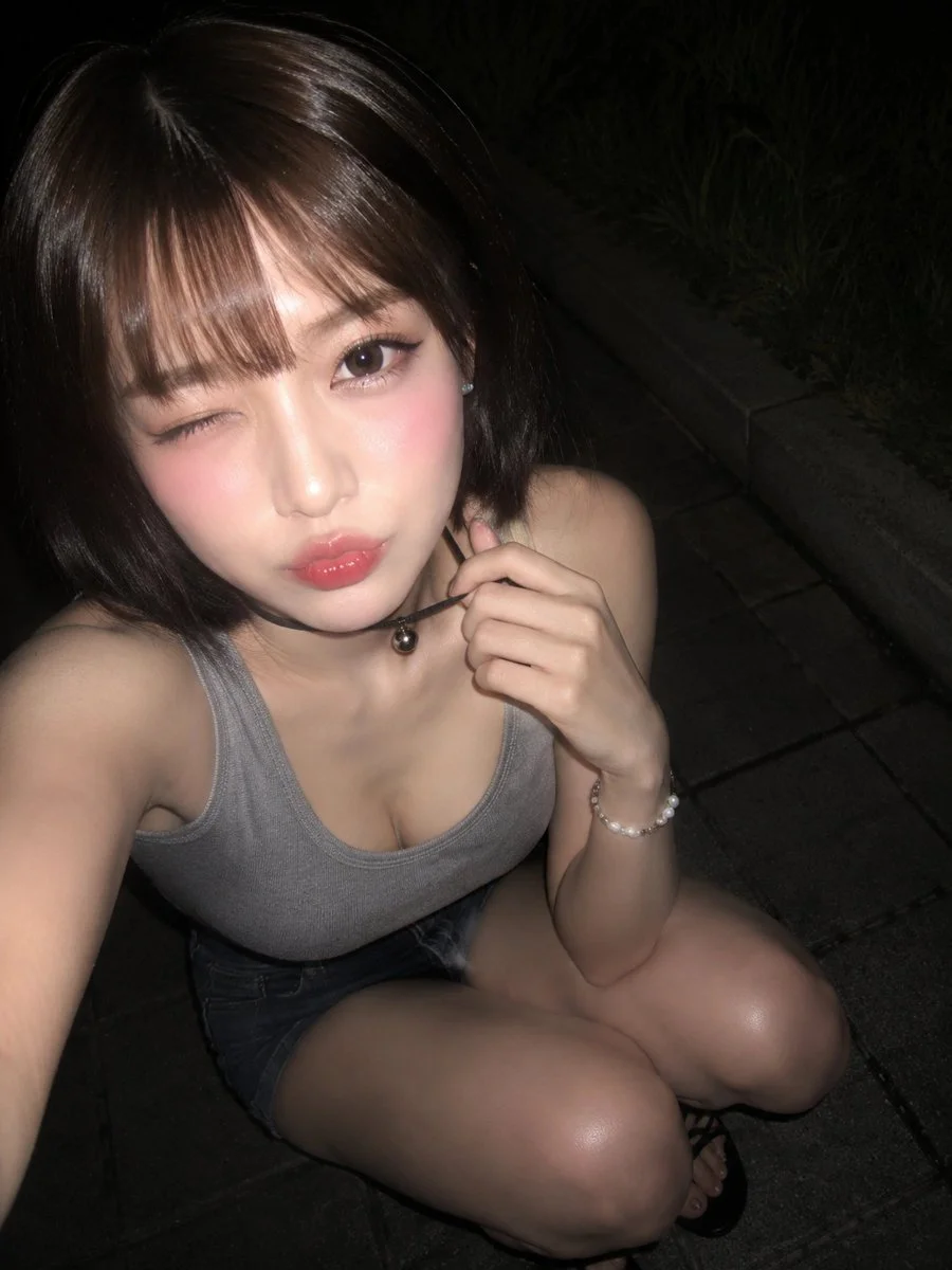 Young woman winks in a nighttime flash selfie crouching on sidewalk