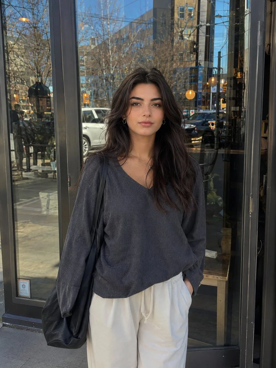 Young woman with dark hair stands outside a modern café in daylight.