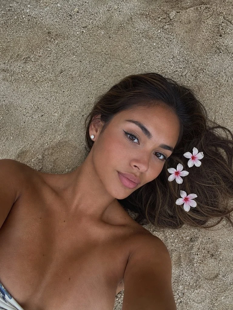 Young woman with tropical flowers lies on warm beach sand